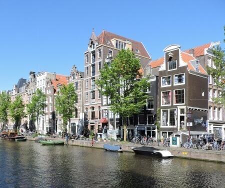 Grachtenhäuser entlang der Amsterdamer Grachten mit Booten an einem sonnigen Tag.