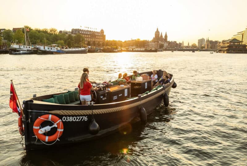 Offenes Boot mit Skipper bei Sonnenuntergang auf den Amsterdamer Grachten