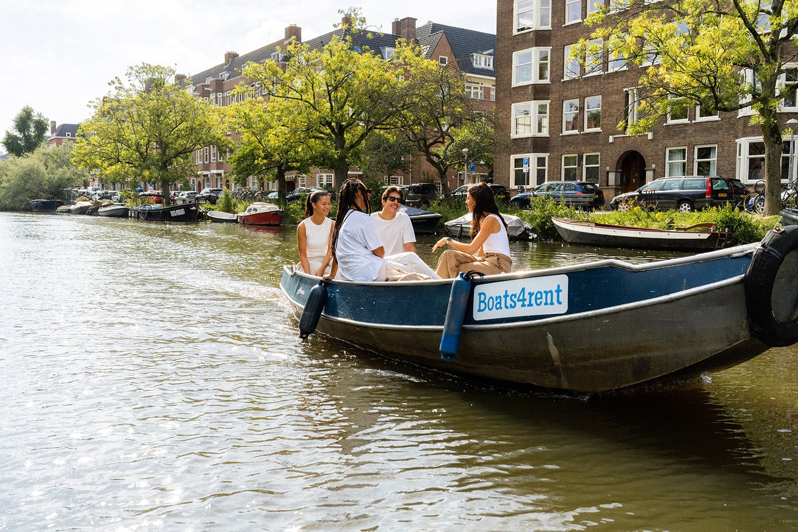 Drei Frauen und ein Mann segeln auf einer Schaluppe durch die Amsterdamer Grachten.